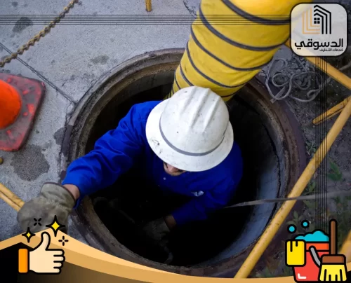 خدمات شركة تسليك مجاري ابوظبي 0545473541 الدسوقي عامل تنظيف المجاري في أبوظبي يباشر العمل داخل فتحة الصرف الصحي، مرتديًا معدات الأمان اللازمة.
