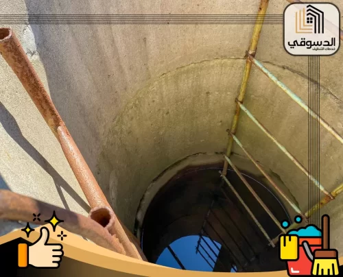 تسليك المجاري بالاسيد راس الخيمة 0545473541 الدسوقي فتحة بيارة خرسانية عميقة يظهر بداخلها ماء راكد وسلالم معدنية مثبتة على الجدار الداخلي.