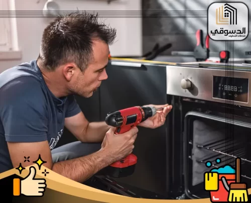 تصليح ميكروويف في العين 0545473541 الدسوقي فني يفحص فرنًا منزليًا مفتوحًا ويجري صيانة دقيقة باستخدام مثقاب كهربائي